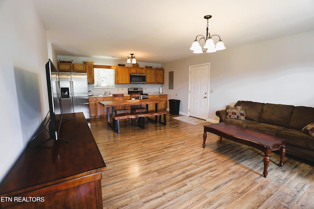 living room with light wood-style flooring, a chandelier, baseboards, and electric panel