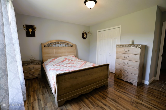 bedroom with dark wood-type flooring, a closet, and baseboards