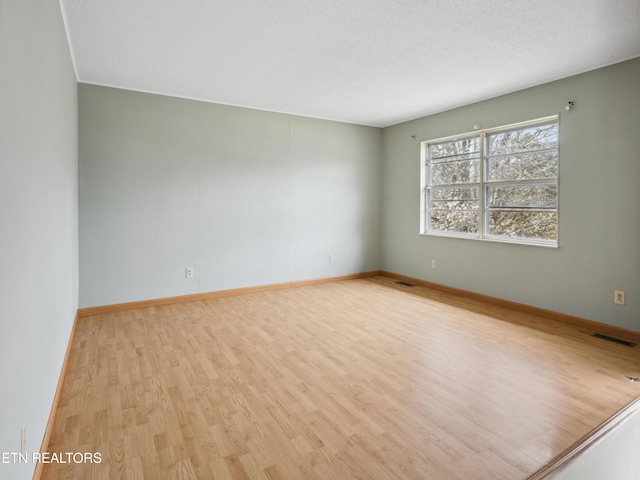 unfurnished room featuring wood finished floors, visible vents, and baseboards