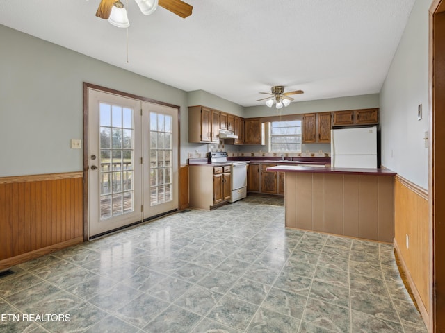 kitchen with white appliances, wainscoting, wood walls, and ceiling fan