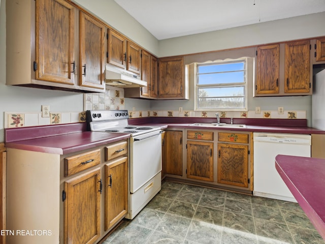 kitchen with a sink, under cabinet range hood, dark countertops, white appliances, and brown cabinetry