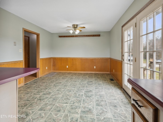 spare room with a wainscoted wall, wooden walls, and a ceiling fan