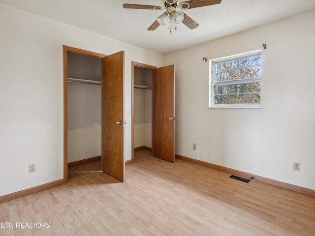 unfurnished bedroom featuring two closets, baseboards, light wood-style floors, and a textured ceiling