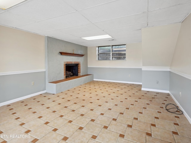 interior space with tile patterned flooring, a fireplace with raised hearth, a paneled ceiling, and baseboards