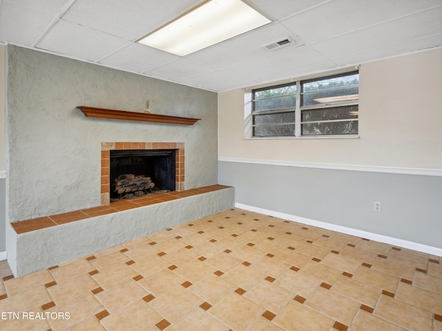 basement with a drop ceiling, a fireplace with raised hearth, visible vents, and baseboards