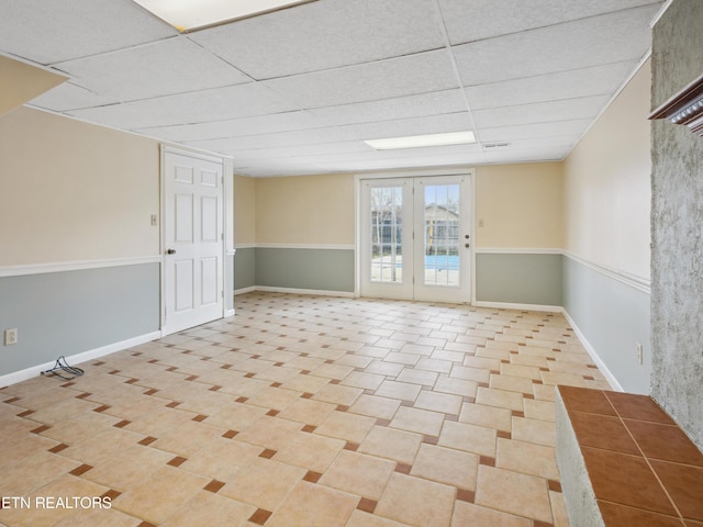 spare room with light tile patterned flooring, french doors, baseboards, and a drop ceiling