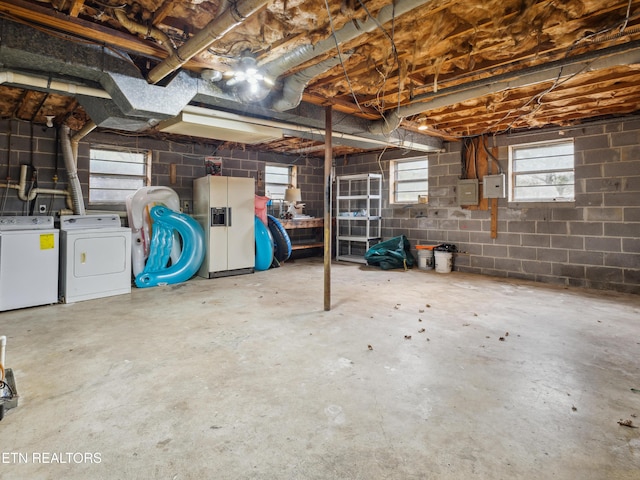 below grade area featuring concrete block wall, white fridge with ice dispenser, and washing machine and clothes dryer