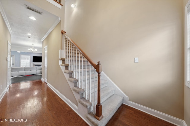 staircase featuring ornamental molding, visible vents, baseboards, and hardwood / wood-style flooring