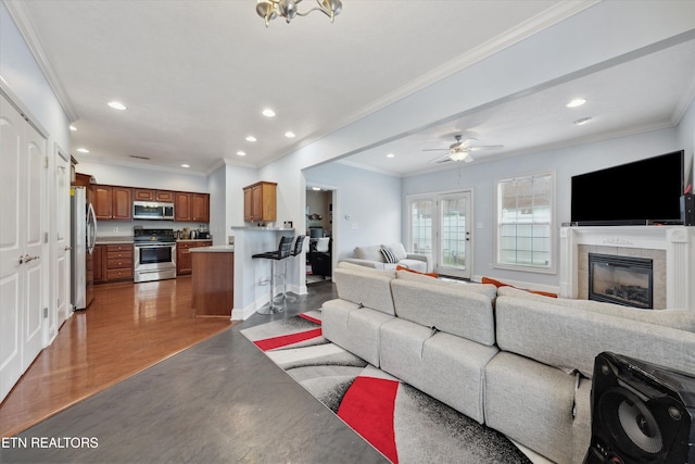 living room featuring recessed lighting, a tiled fireplace, light wood-style floors, ornamental molding, and a ceiling fan