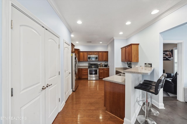 kitchen featuring brown cabinets, appliances with stainless steel finishes, ornamental molding, a peninsula, and a kitchen breakfast bar