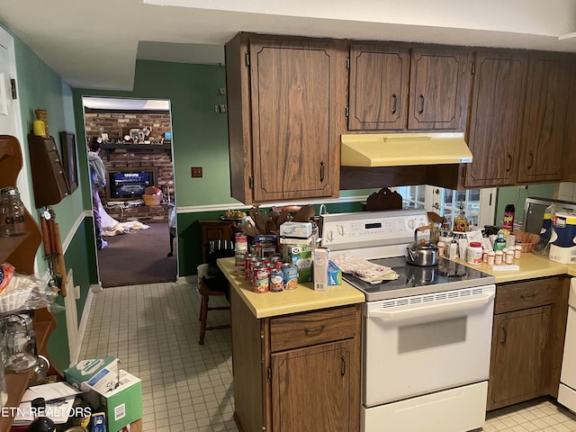 kitchen with a brick fireplace, under cabinet range hood, white range with electric stovetop, and light countertops