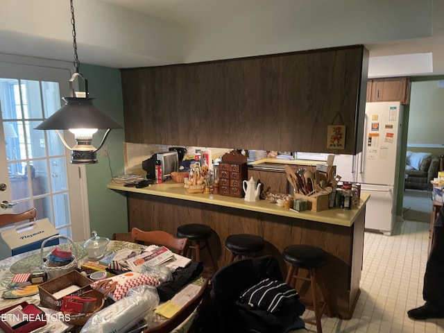 kitchen featuring pendant lighting, light countertops, freestanding refrigerator, a peninsula, and a kitchen bar