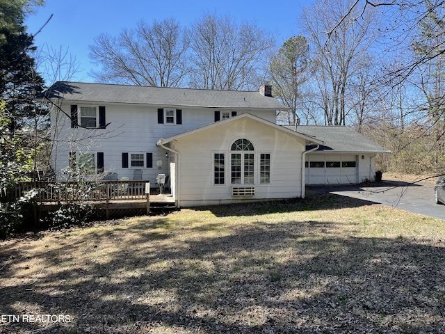 back of property featuring roof with shingles, a chimney, a lawn, an attached garage, and a deck