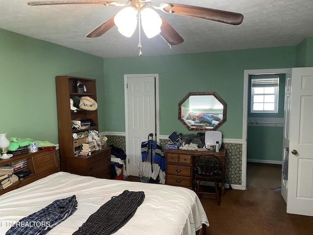 carpeted bedroom with a ceiling fan, wainscoting, and a textured ceiling