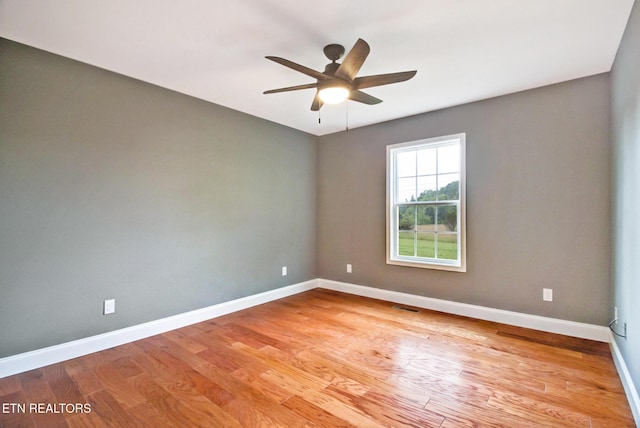 spare room featuring light wood-type flooring, ceiling fan, visible vents, and baseboards