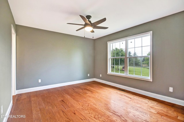 spare room featuring a ceiling fan, visible vents, baseboards, and wood finished floors