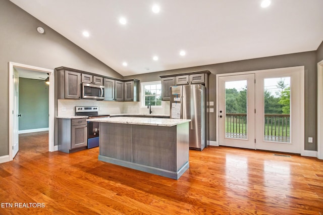 kitchen featuring tasteful backsplash, a kitchen island, stainless steel appliances, light wood-type flooring, and a sink