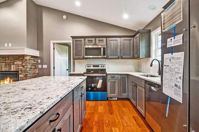 kitchen featuring a stone fireplace, stainless steel appliances, wood finished floors, a sink, and vaulted ceiling