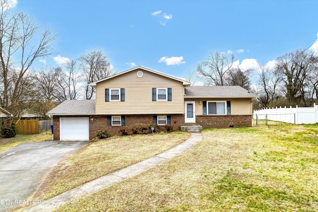 tri-level home featuring an attached garage, brick siding, fence, driveway, and a front yard