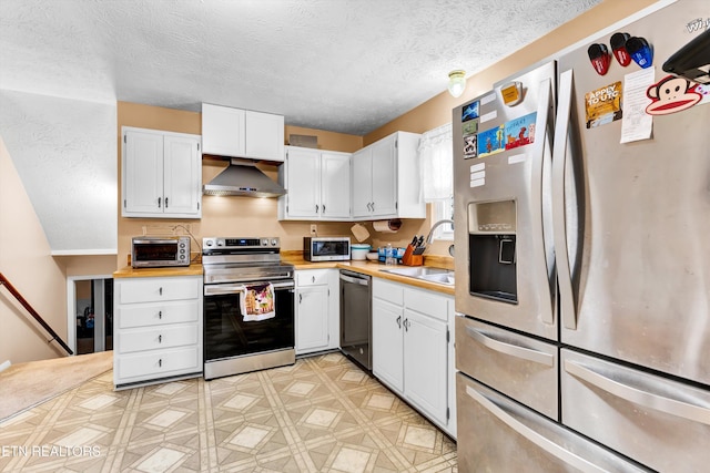 kitchen featuring wall chimney exhaust hood, appliances with stainless steel finishes, a sink, and light countertops