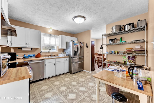 kitchen with stainless steel appliances, a textured ceiling, light floors, white cabinetry, and a sink