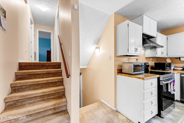 kitchen featuring a toaster, wall chimney exhaust hood, a textured ceiling, white cabinetry, and range with electric stovetop