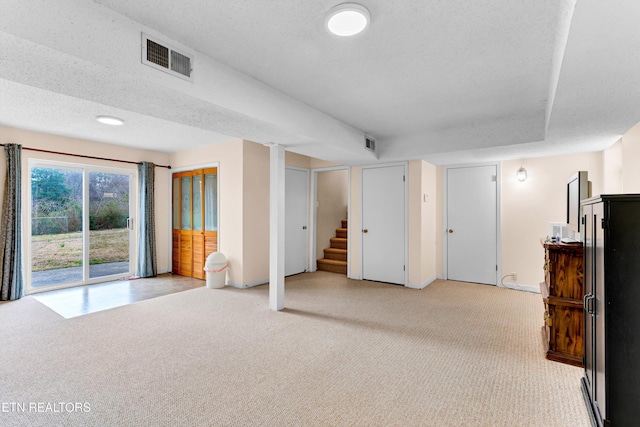 basement featuring stairs, a textured ceiling, visible vents, and light colored carpet