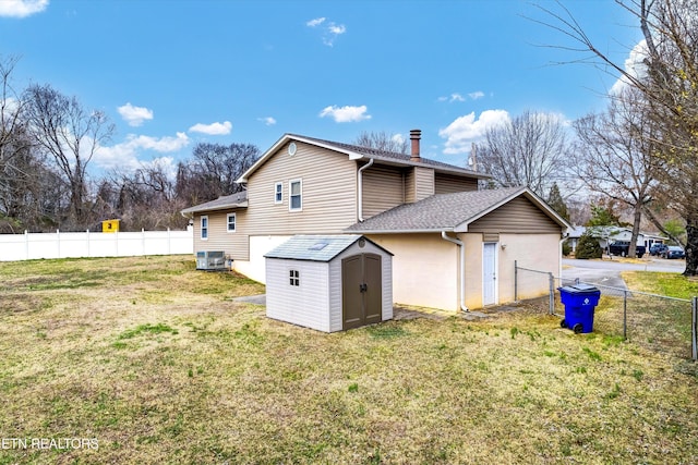 back of property with an outbuilding, a storage unit, a lawn, and fence