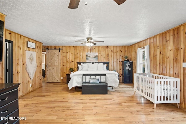 unfurnished bedroom with light wood-style floors, a barn door, a textured ceiling, and wood walls