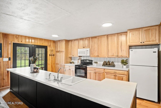 kitchen with wooden walls, white appliances, a sink, light countertops, and light wood finished floors