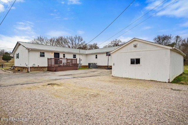 rear view of house featuring driveway, metal roof, a deck, and central AC