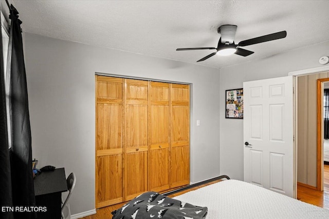 bedroom featuring a ceiling fan, a textured ceiling, baseboards, and wood finished floors