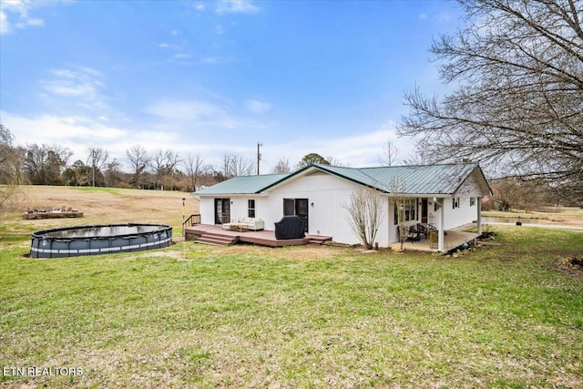 back of house with a covered pool, metal roof, a lawn, and a wooden deck