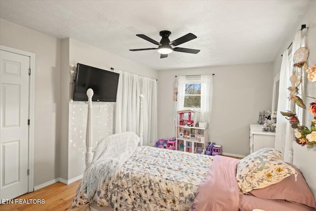 bedroom featuring a textured ceiling, light wood finished floors, a ceiling fan, and baseboards