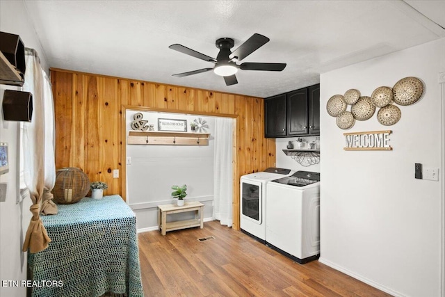 kitchen featuring washer and clothes dryer, light wood finished floors, ceiling fan, wooden walls, and dark cabinets