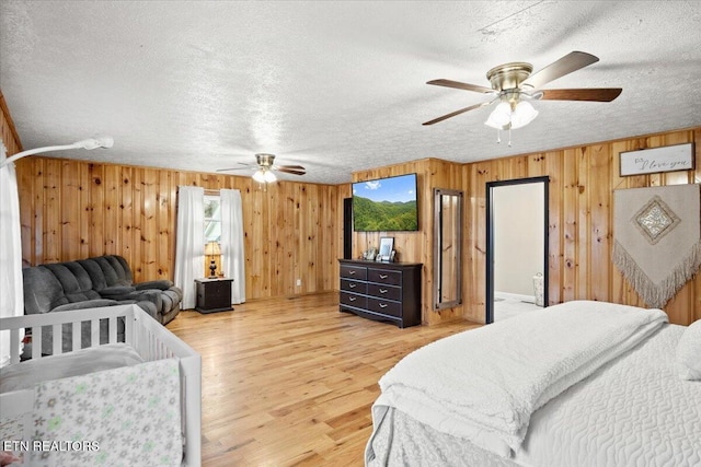 bedroom featuring light wood-style floors, a ceiling fan, a textured ceiling, and wood walls