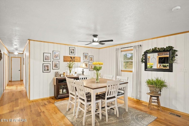 dining area with a textured ceiling, a ceiling fan, visible vents, light wood-style floors, and crown molding