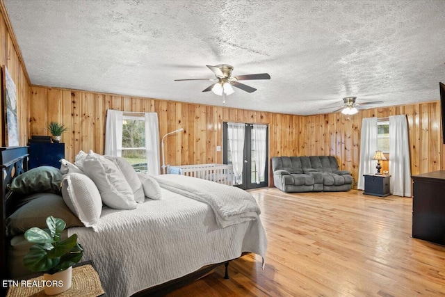 bedroom with light wood-style floors, wooden walls, a ceiling fan, and a textured ceiling