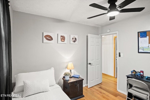 bedroom with light wood-type flooring, ceiling fan, baseboards, and a textured ceiling