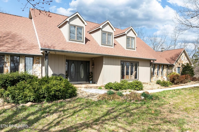 cape cod home featuring stone siding, a shingled roof, and a front yard