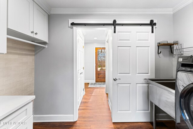 laundry area with a barn door, ornamental molding, wood finished floors, cabinet space, and washer / clothes dryer