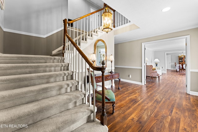 stairs featuring a notable chandelier, ornamental molding, baseboards, and wood finished floors