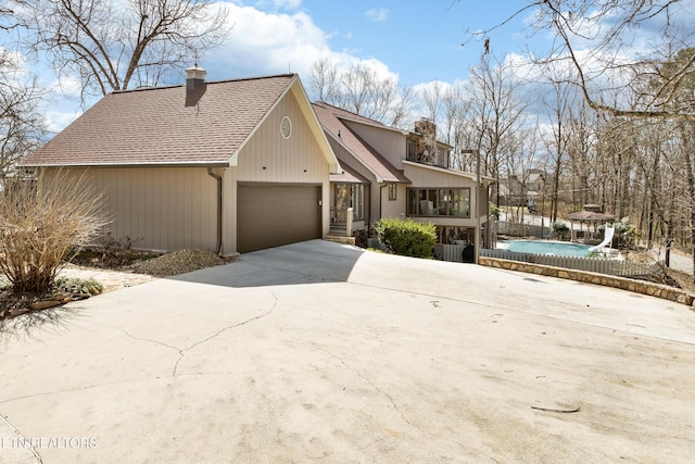 rustic home with a fenced in pool, an attached garage, concrete driveway, and a chimney