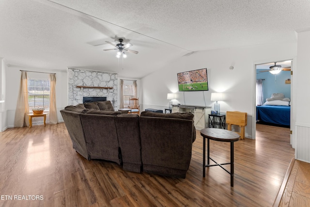 living area featuring vaulted ceiling, a fireplace, ceiling fan, and wood finished floors
