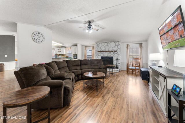 living area featuring wood finished floors, lofted ceiling, a fireplace, ceiling fan, and a textured ceiling