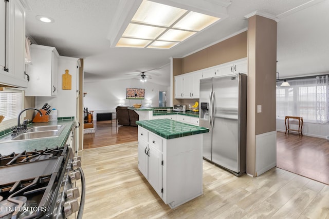 kitchen featuring a sink, vaulted ceiling, tile counters, stainless steel fridge, and light wood-type flooring