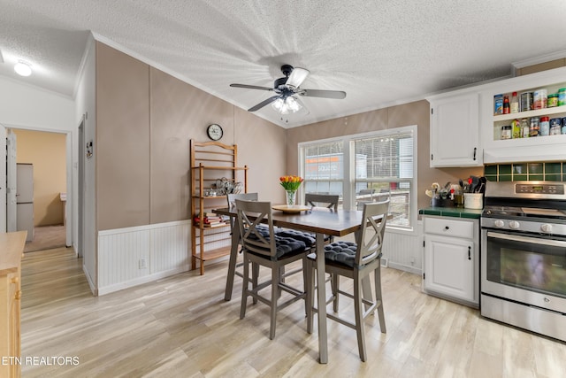 dining area with a textured ceiling, ornamental molding, a ceiling fan, and light wood finished floors