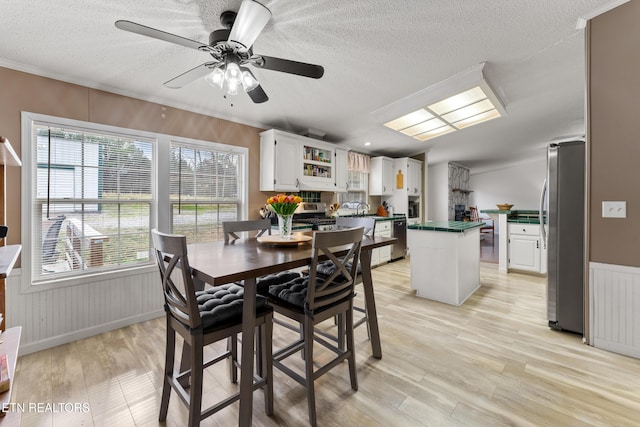 dining space with light wood finished floors, ornamental molding, wainscoting, a textured ceiling, and a ceiling fan