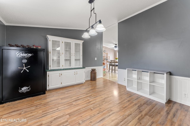 unfurnished dining area with a wainscoted wall, a ceiling fan, light wood-type flooring, and ornamental molding