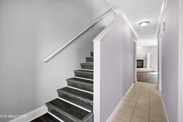 stairs with baseboards, crown molding, a tiled fireplace, and tile patterned floors